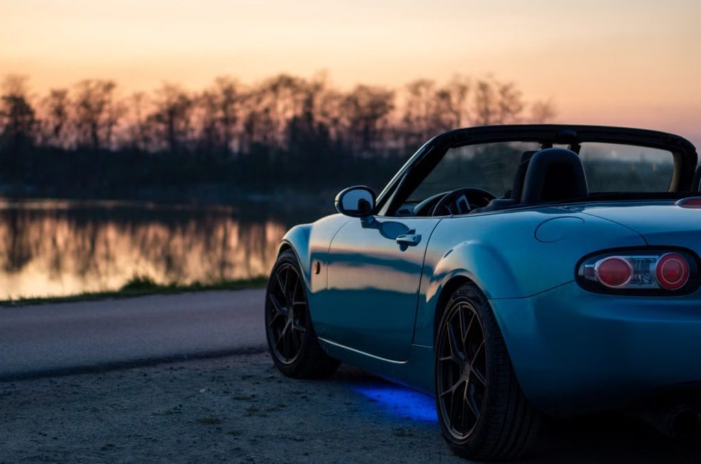 A sports car parked by a lake at sunset in Brzegi, Poland, offering a scenic view.