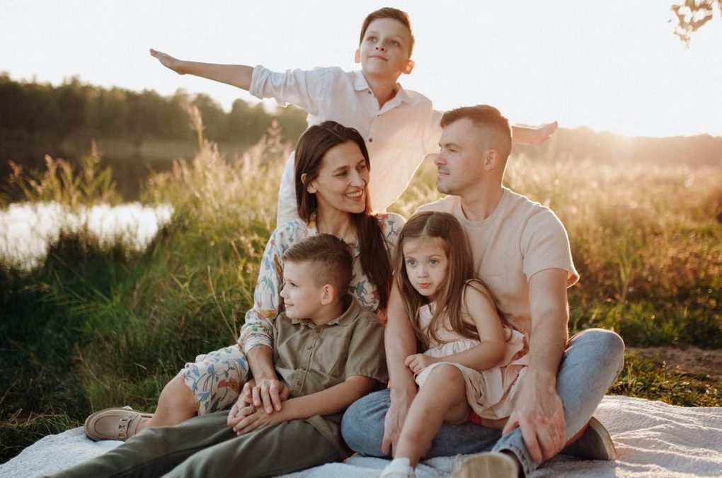 A family of five enjoying a serene picnic in a sunlit meadow during sunset.