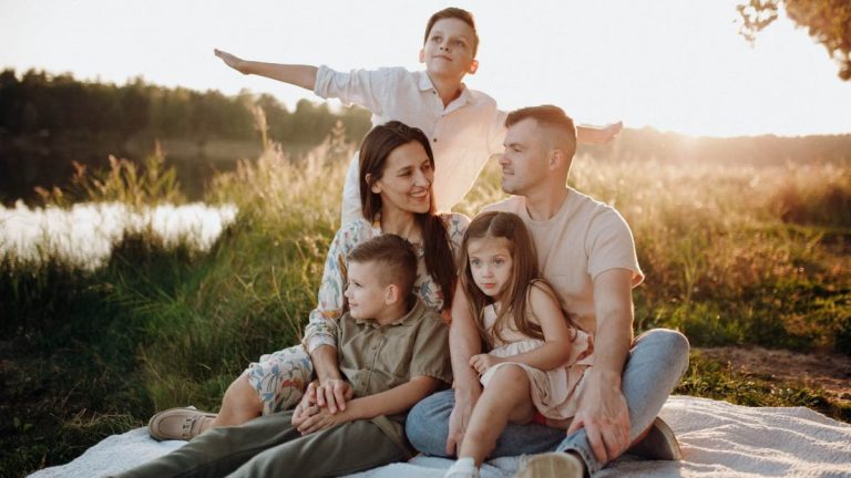 A family of five enjoying a serene picnic in a sunlit meadow during sunset.