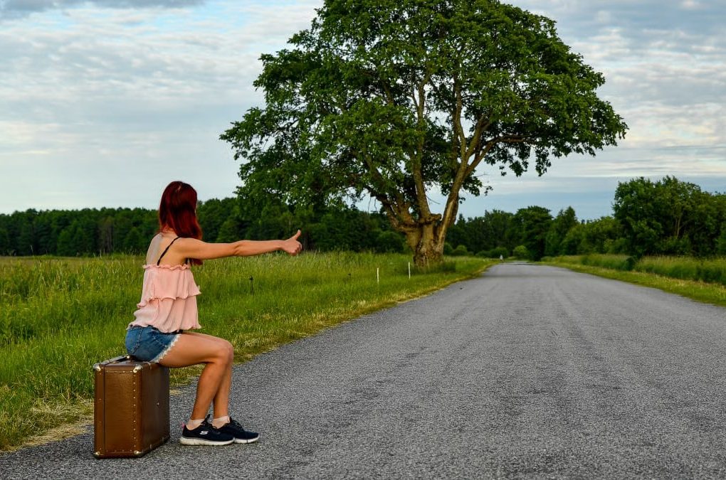 A woman hitchhikes on a rural road in Kolga, Estonia, seeking travel adventures.